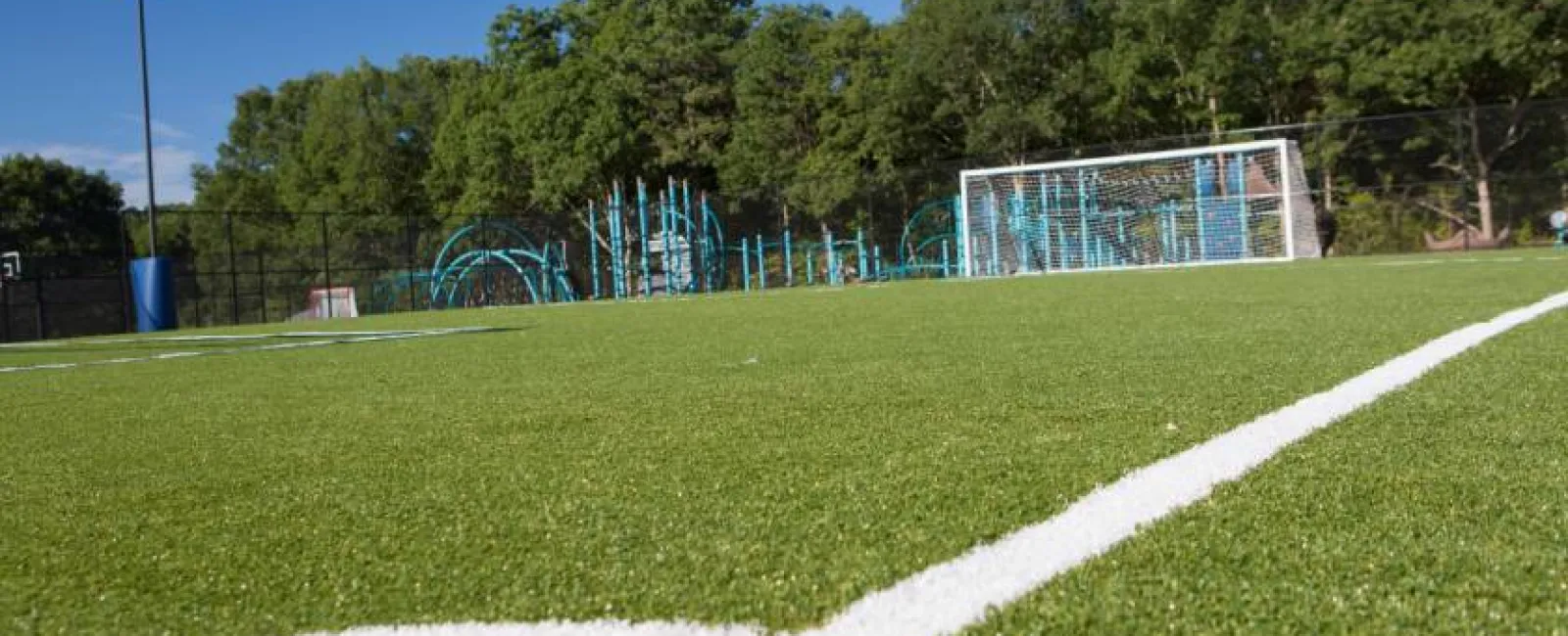 Low angle view of soccer field with white lines, goalpost, playground, and trees under clear blue sky.