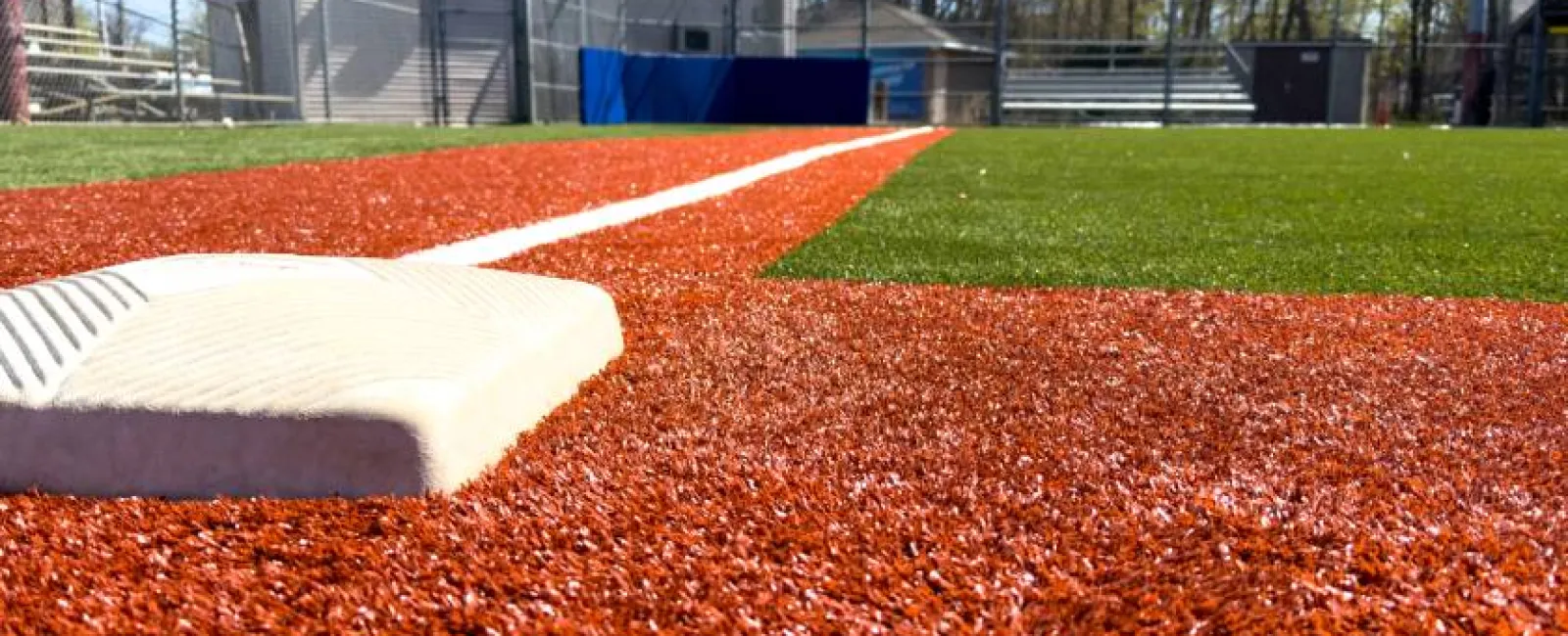 Close-up of a baseball base on a synthetic turf infield with a white foul line extending toward the field.