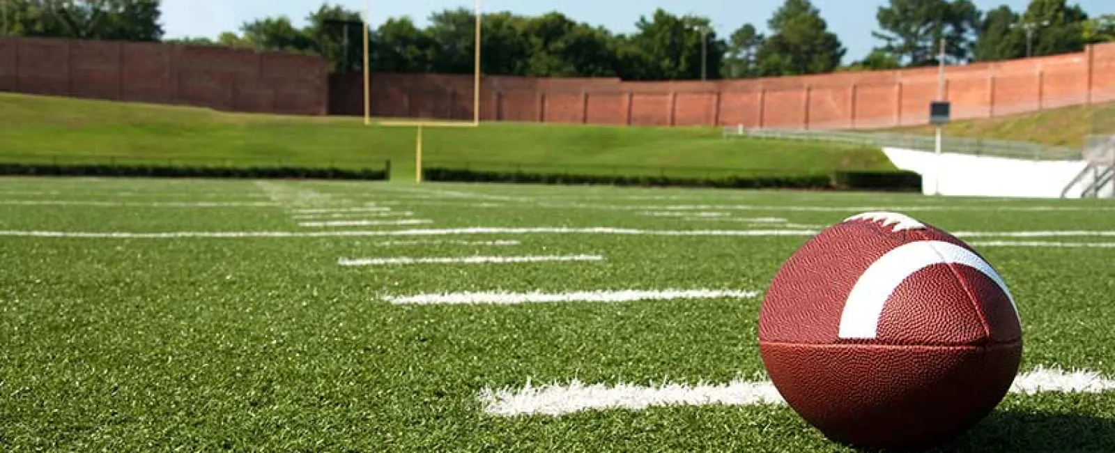 American football resting on green turf near the end zone with goalposts and stadium in background