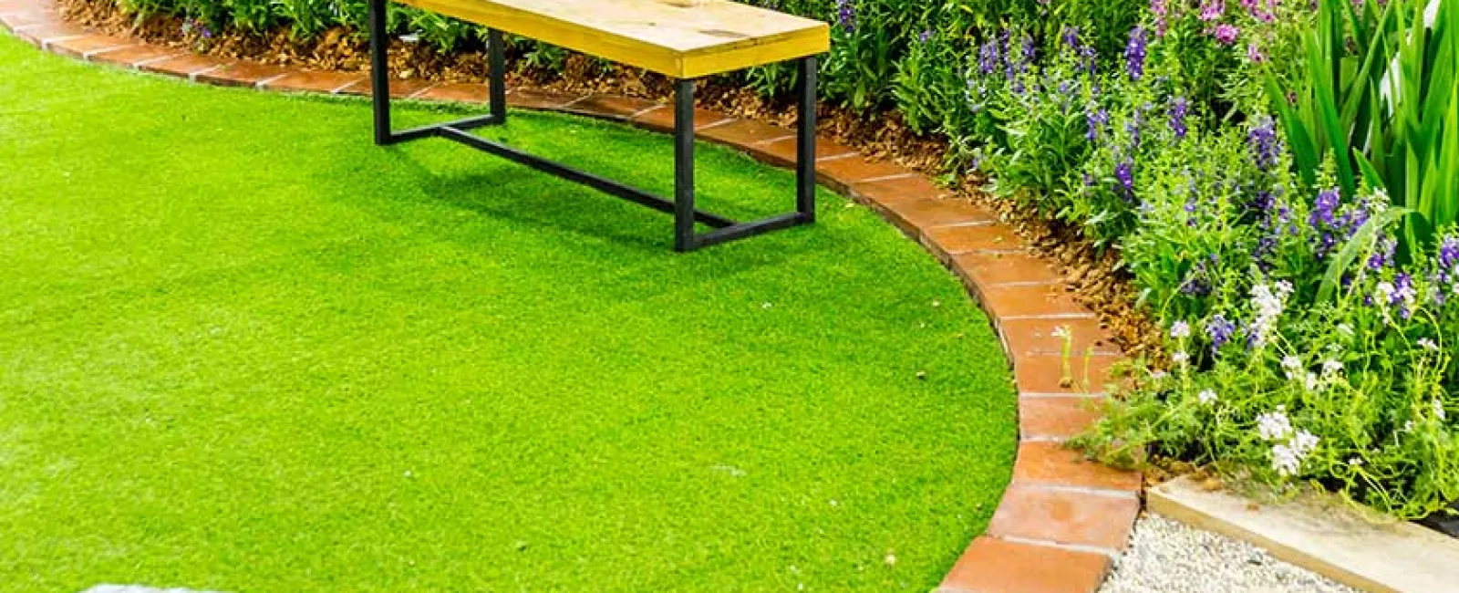 Wooden bench with metal frame on curved green lawn beside colorful flower bed and stone path