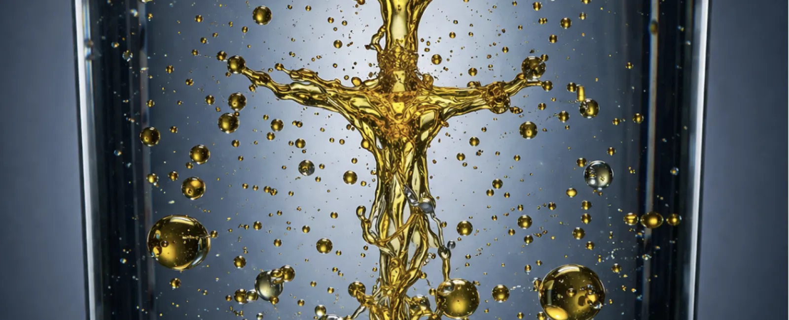 Golden liquid droplets mixing into clear water in a transparent glass, creating dynamic splash patterns and bubbles.