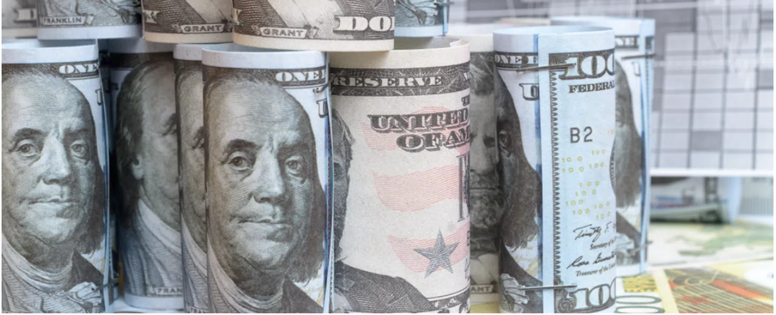 Rolled US dollar bills with financial charts in the background symbolizing investment and economic growth.