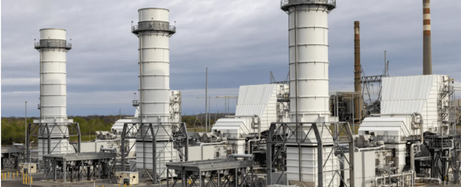 Industrial power plant with large white cooling towers and smokestacks under cloudy sky in daytime