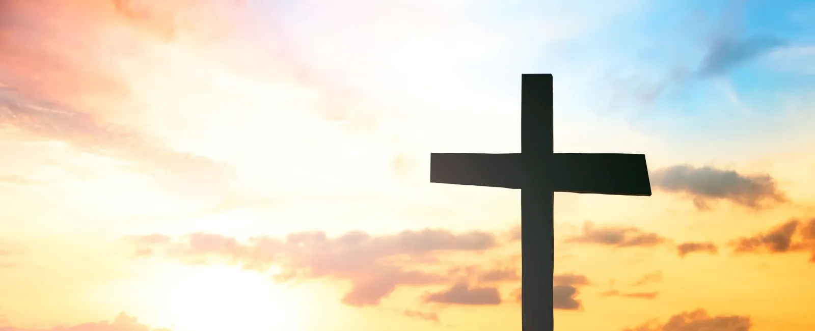 Silhouette of a cross on a hill against a vibrant sunrise with mountains and clouds in the background