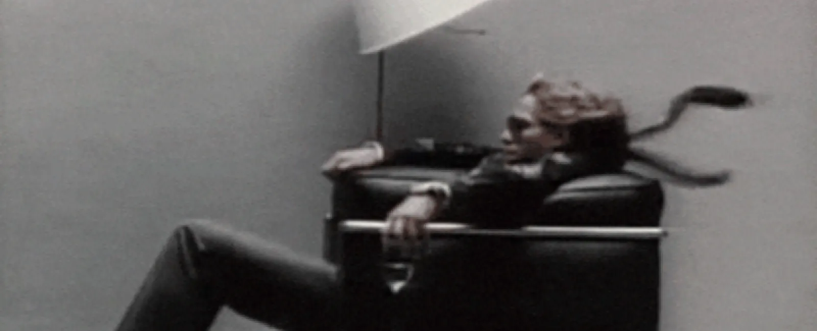 Man in suit reclining on modern black leather chair with tie blowing and lamp in background in minimalist room