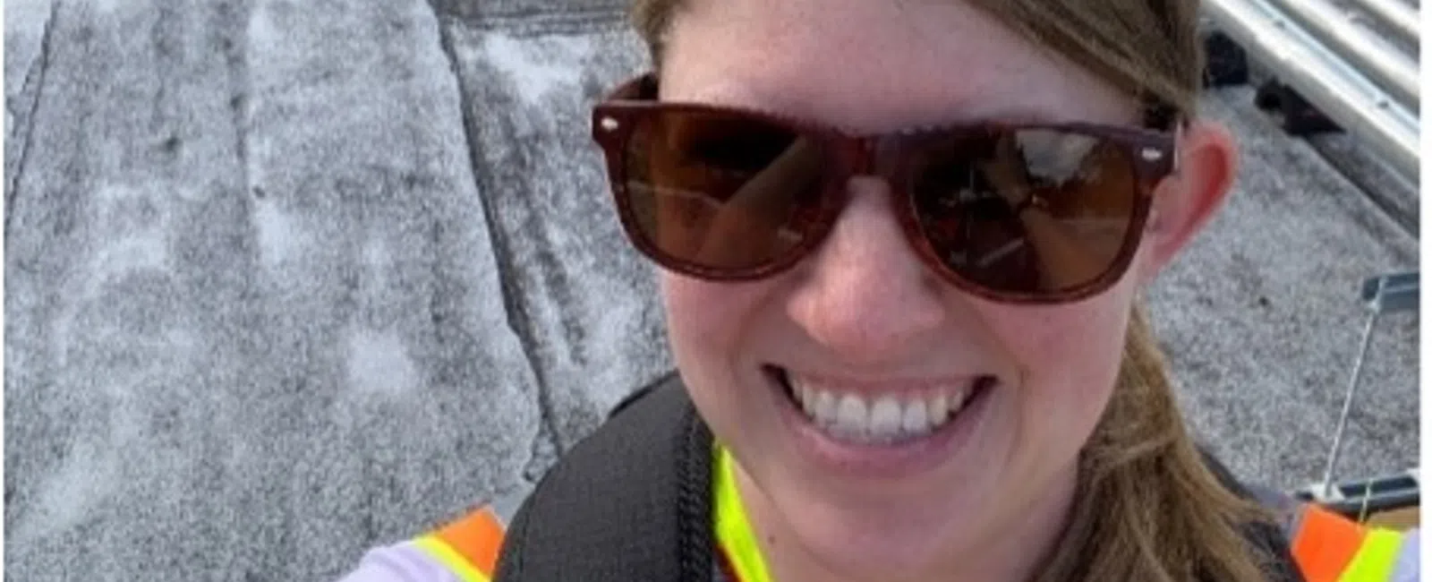 Smiling woman in safety vest and sunglasses takes selfie on industrial rooftop with pipes and equipment in background