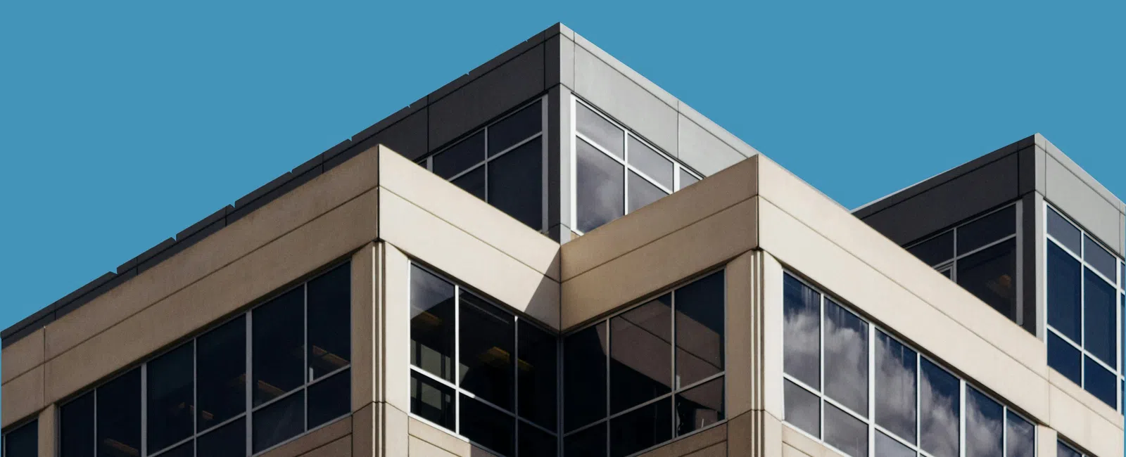 Modern office building corner with large reflective glass windows against clear blue sky.