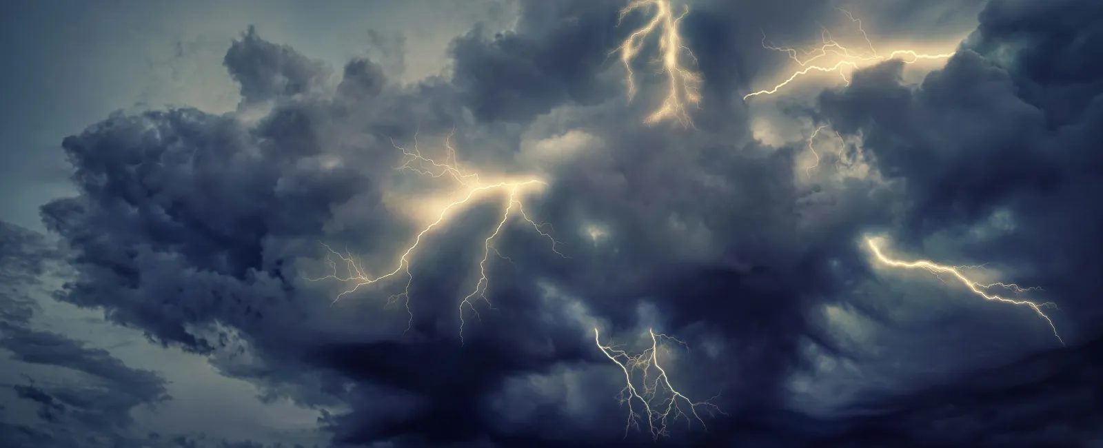 Dark storm clouds illuminated by multiple bright lightning bolts across a turbulent sky at night