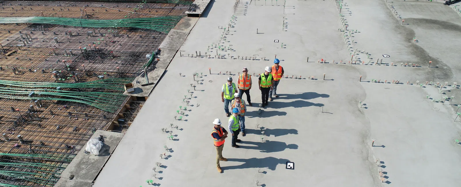 Construction workers in safety gear standing on a concrete foundation slab at a building site under development.