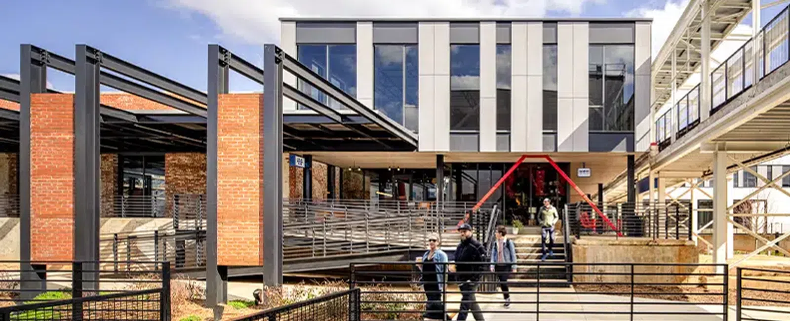 Modern commercial building with glass, brick walls, pedestrian walkways, and people walking outside on a sunny day.