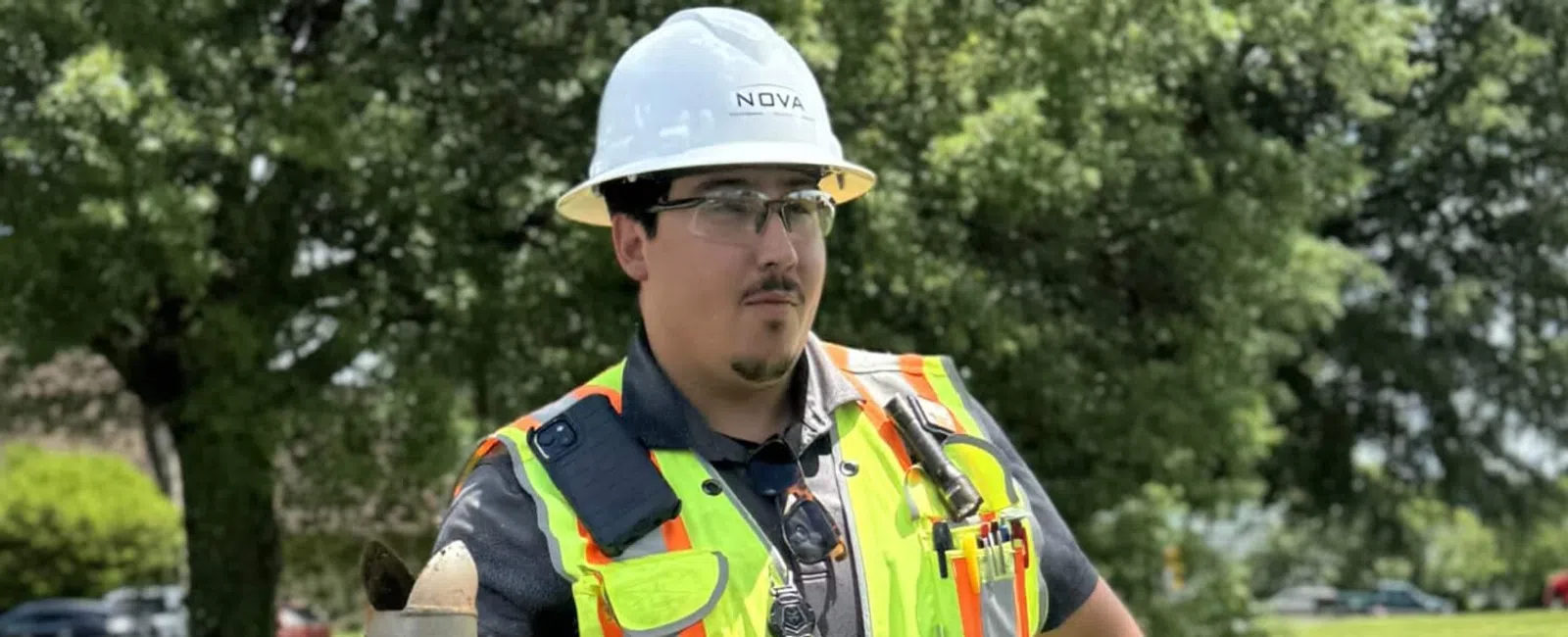 Construction worker in safety gear operating equipment on a grassy outdoor site with trees in background