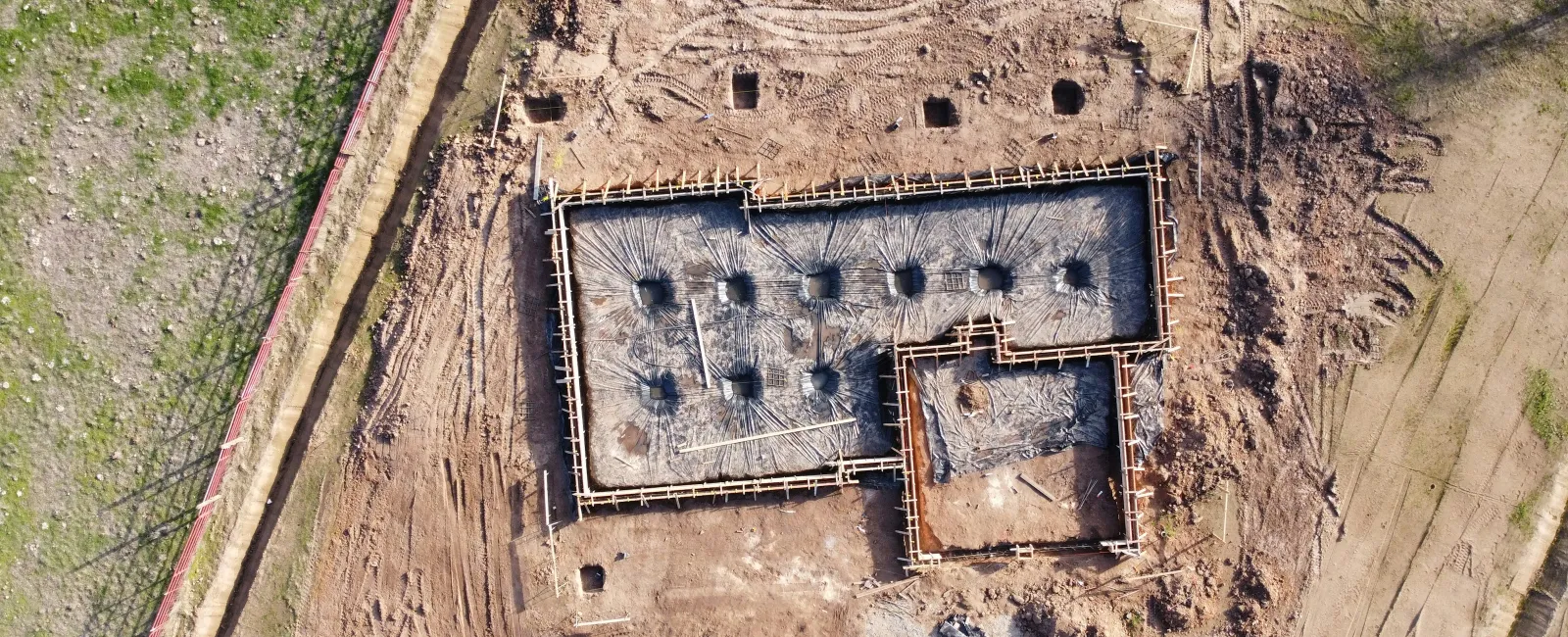 Aerial view of a building foundation under construction with soil excavation and formwork in place.