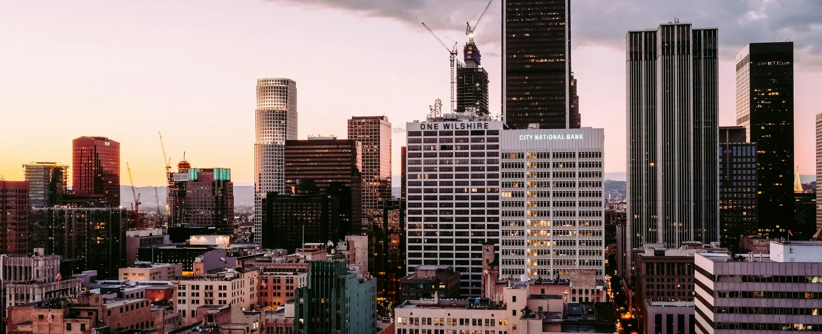 Downtown city skyline at dusk with high-rise buildings and pink cloudy sky in the background.