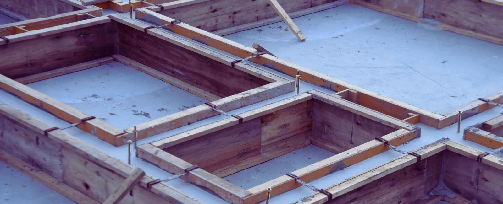Wooden formwork installed on concrete slab for building foundation construction work.