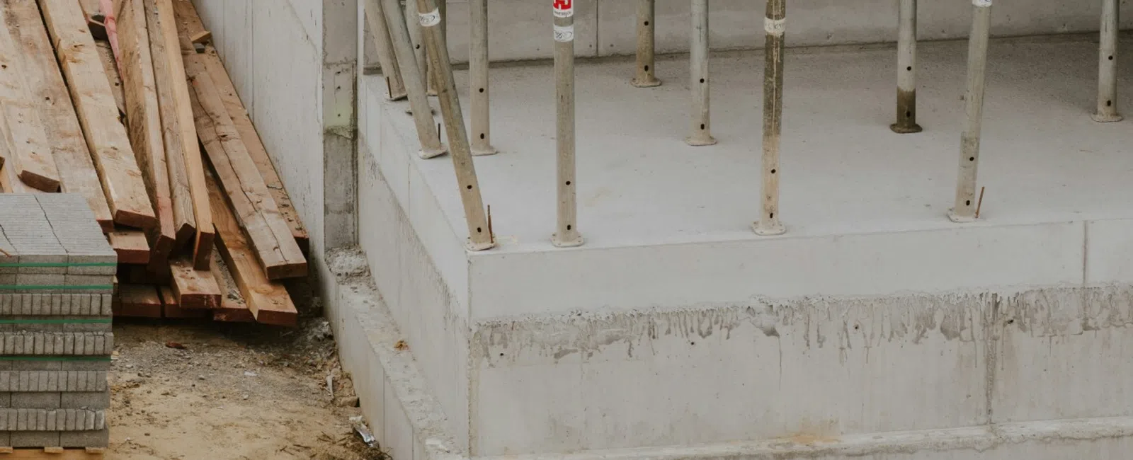 Concrete building under construction with metal scaffolding props and wooden planks on site.