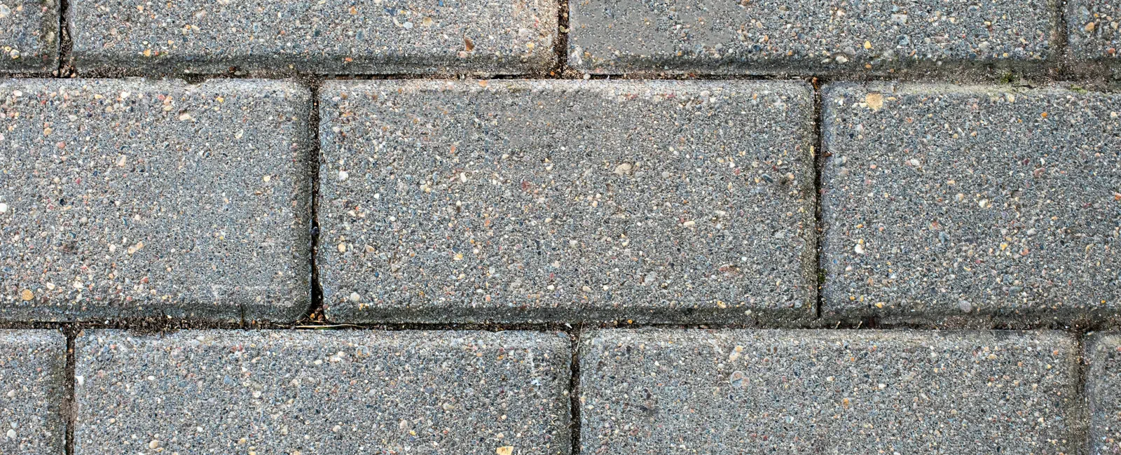 Close-up of textured gray concrete bricks with small colorful stones, arranged in a staggered pattern.