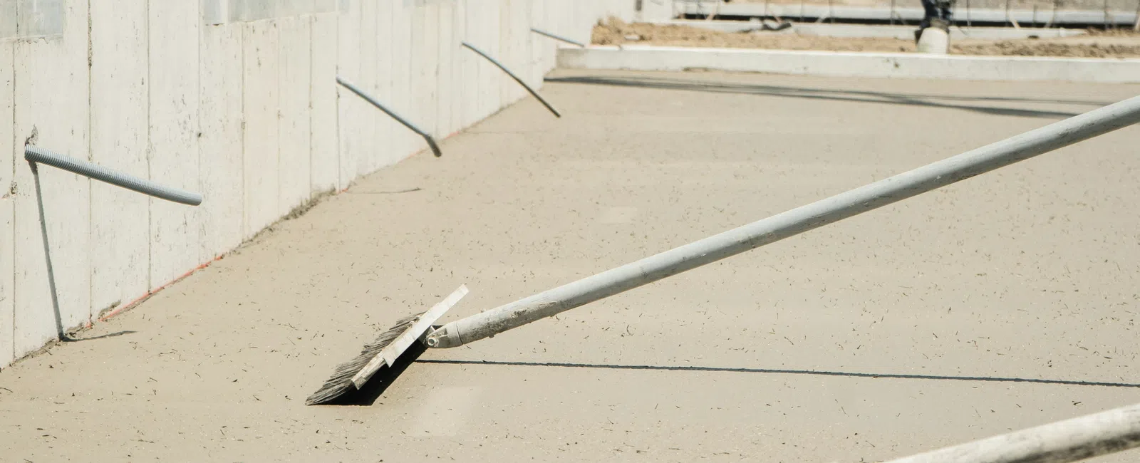Construction workers smoothing freshly poured concrete beside a building on a sunny day.