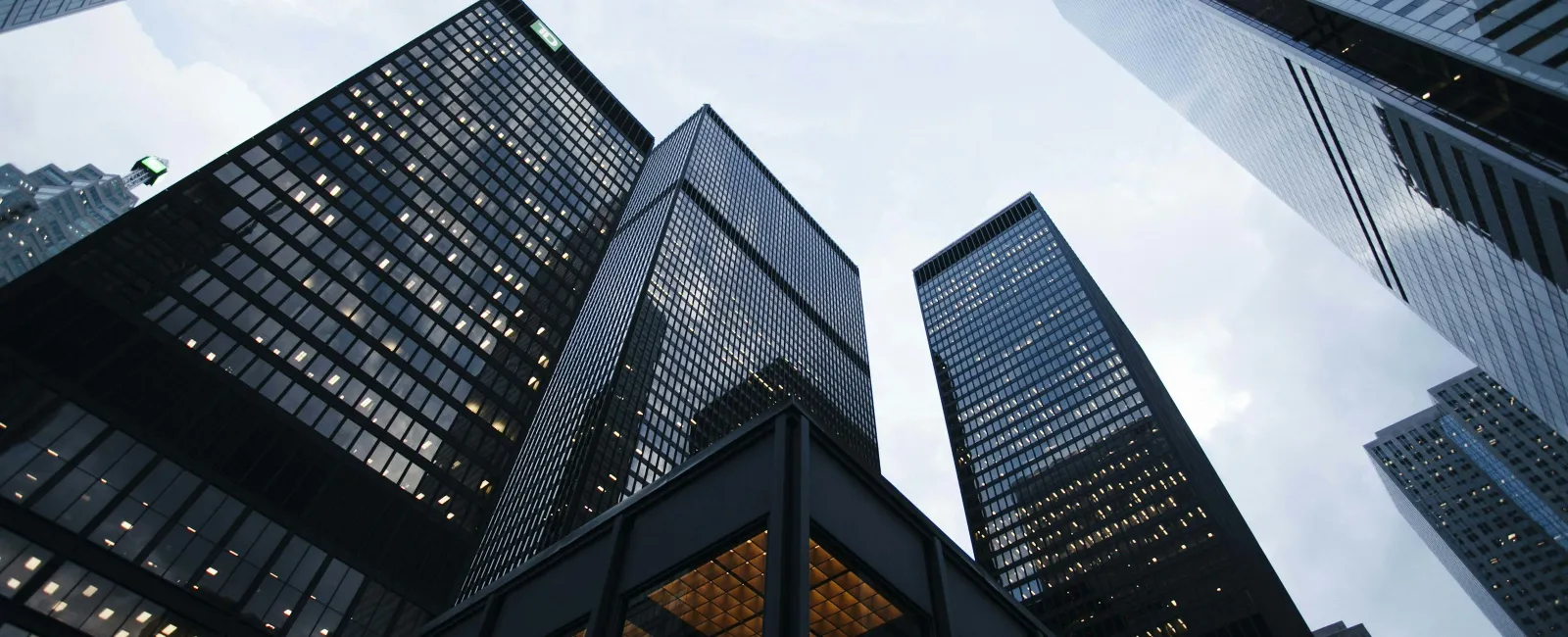 Low-angle view of modern glass skyscrapers with evening lights against a cloudy sky in the city.