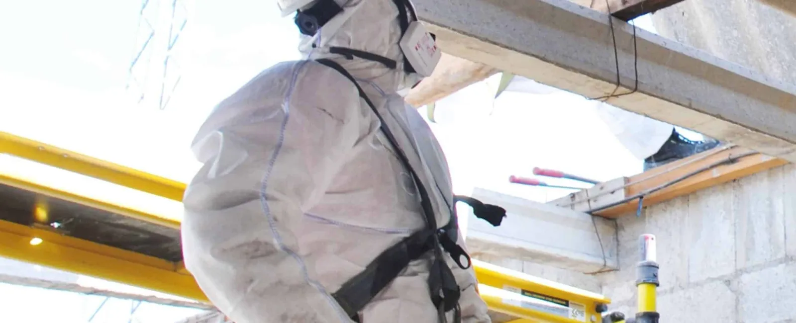 Construction worker in protective gear using bolt cutters on scaffold at a building site under roof beams.