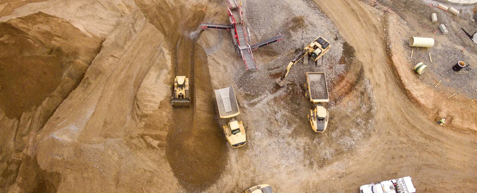 Aerial view of construction site with trucks, excavators, conveyor belt, and dirt piles during earthmoving work