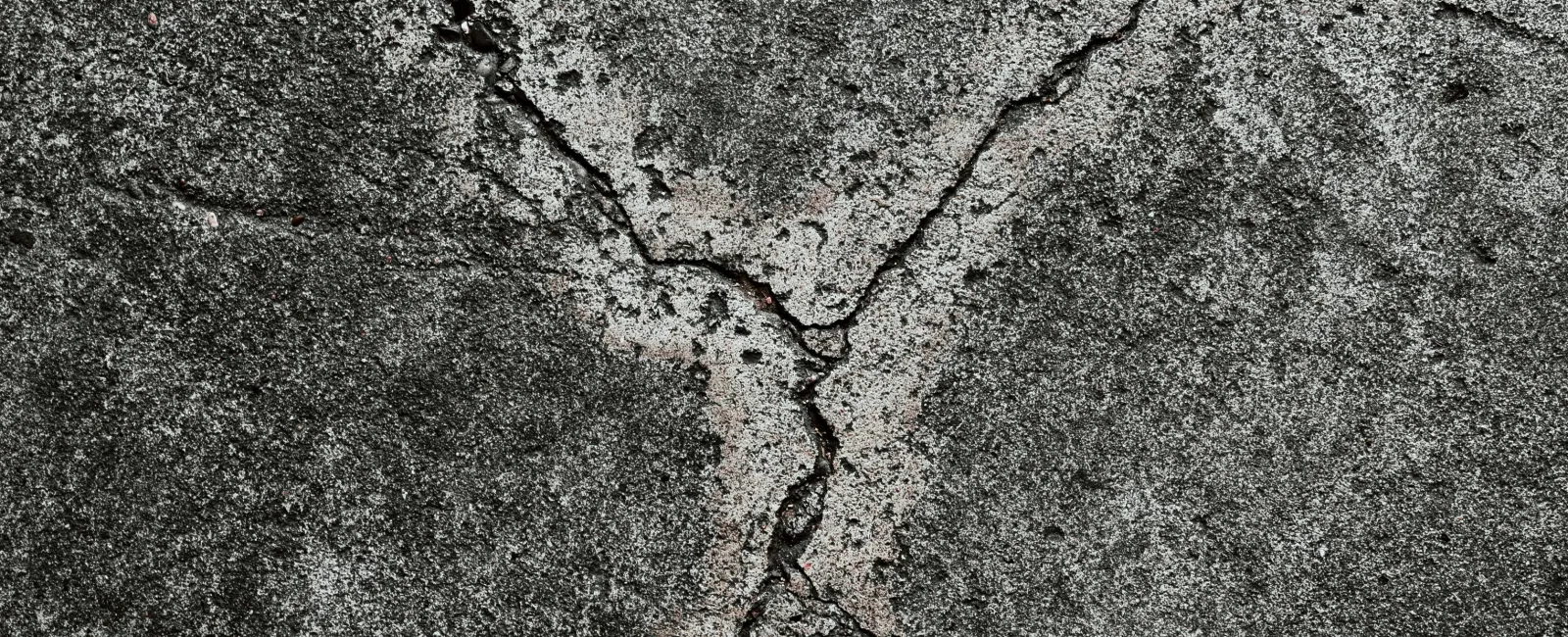 Close-up of dark gray cracked concrete surface showing textured roughness and fracture lines