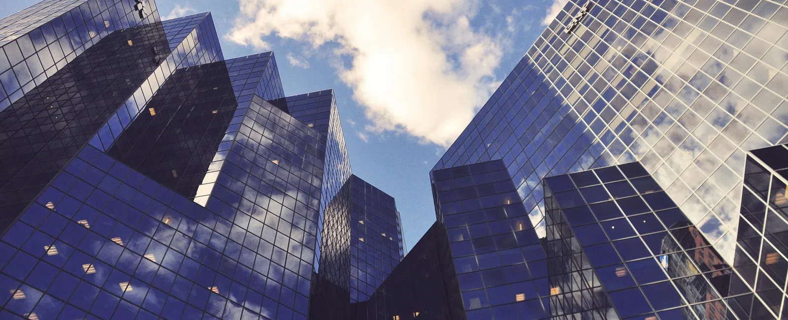 Reflective glass skyscrapers under a partly cloudy blue sky in a modern cityscape.