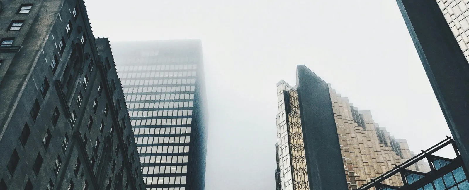 Foggy sky above tall city skyscrapers with glass and concrete facades reflecting light and shadows.