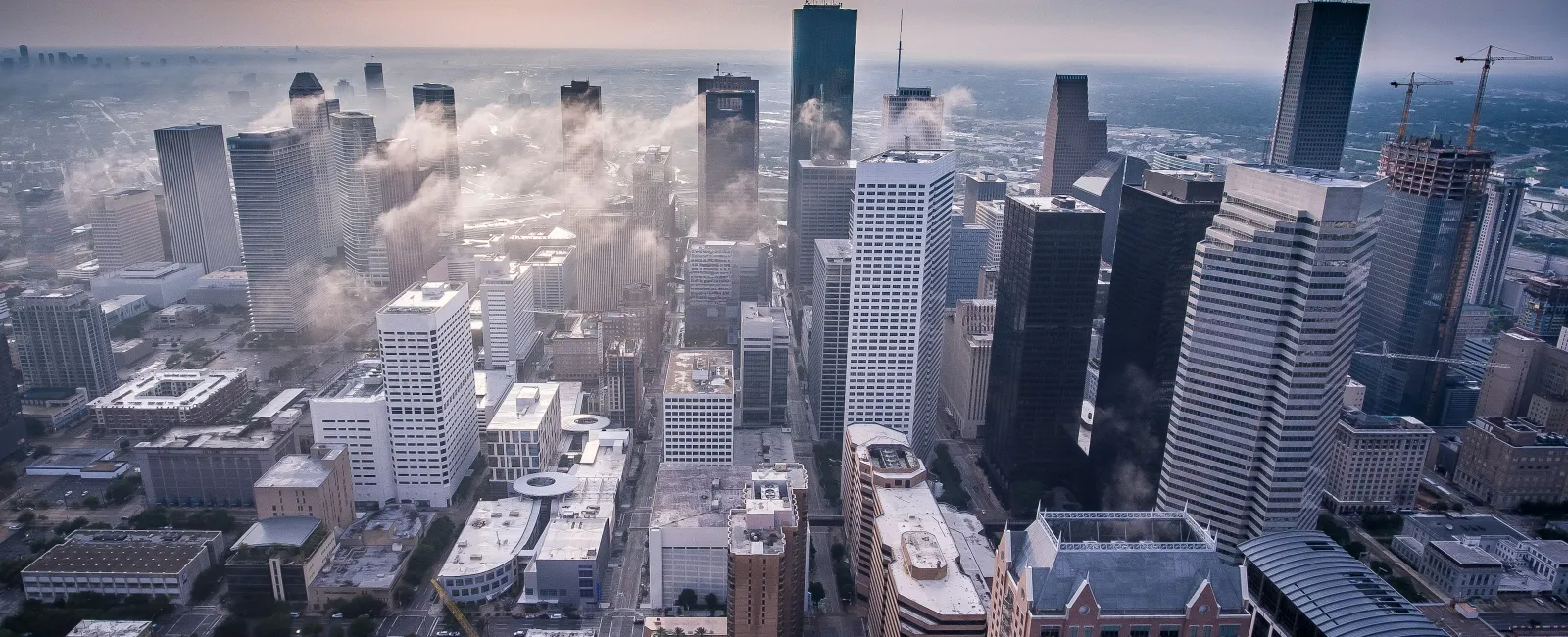 Aerial view of a city skyline with skyscrapers and foggy atmosphere during sunrise or sunset