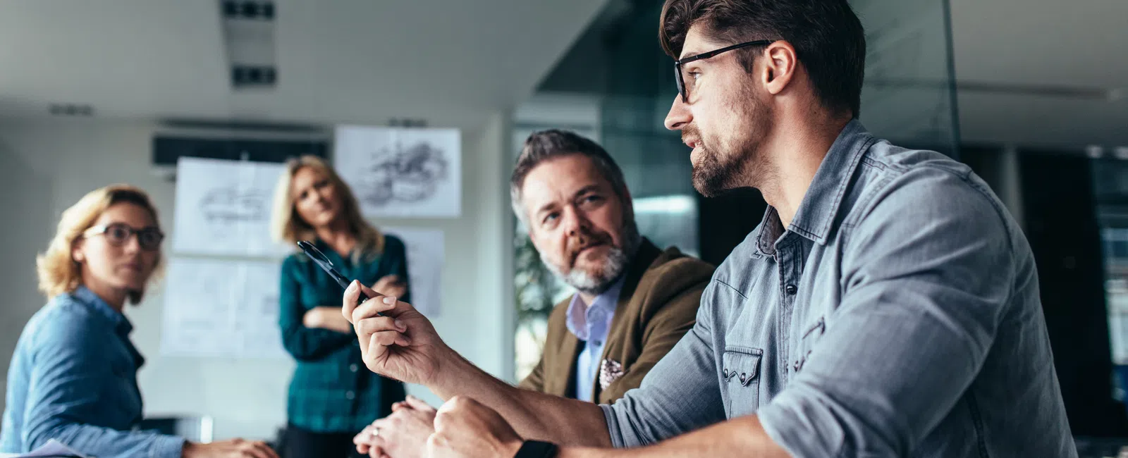 Four professionals engaged in a discussion during a meeting in a modern office setting with architectural sketches.
