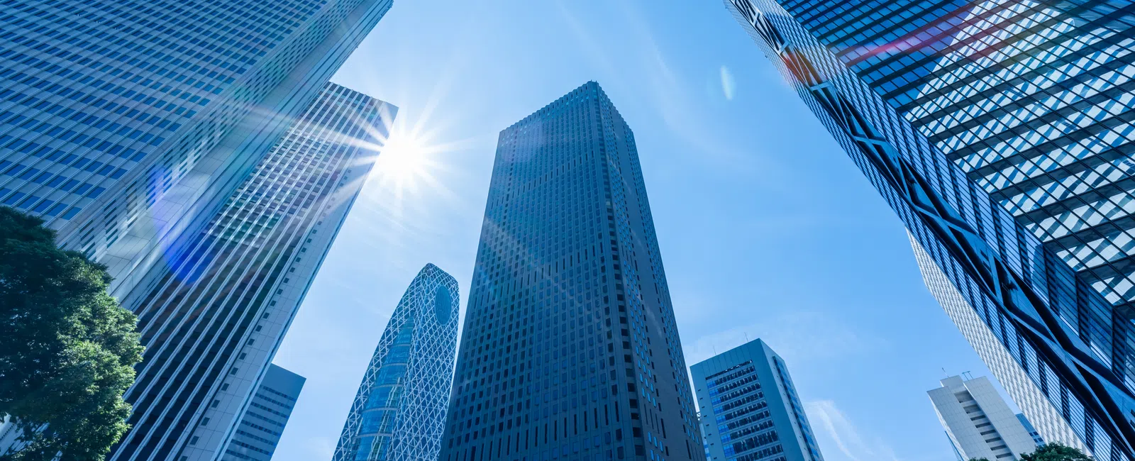 Sun shining brightly among tall modern skyscrapers in a clear blue sky urban cityscape.