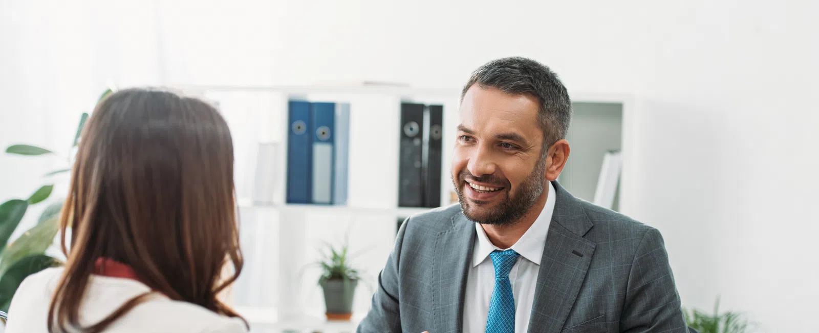 Businessman in suit smiling and discussing work with colleague in office meeting over laptop.