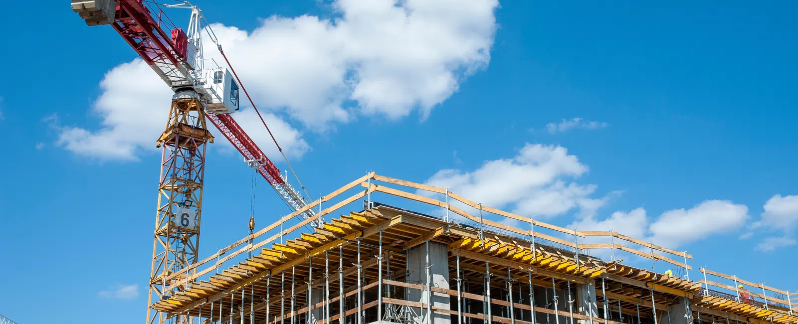 Construction site with a building framework and a tall red and white crane under a blue sky with clouds
