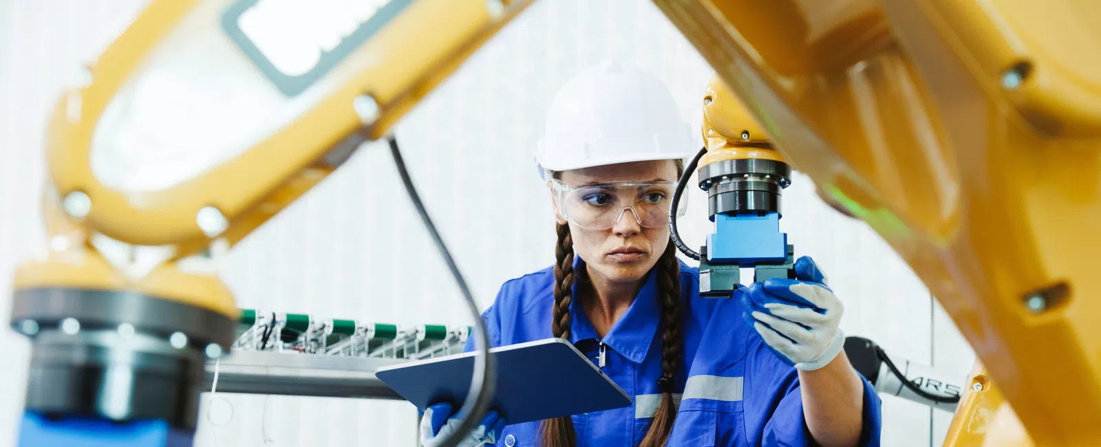 Female engineer in safety gear programming an industrial robotic arm in a modern factory setting.