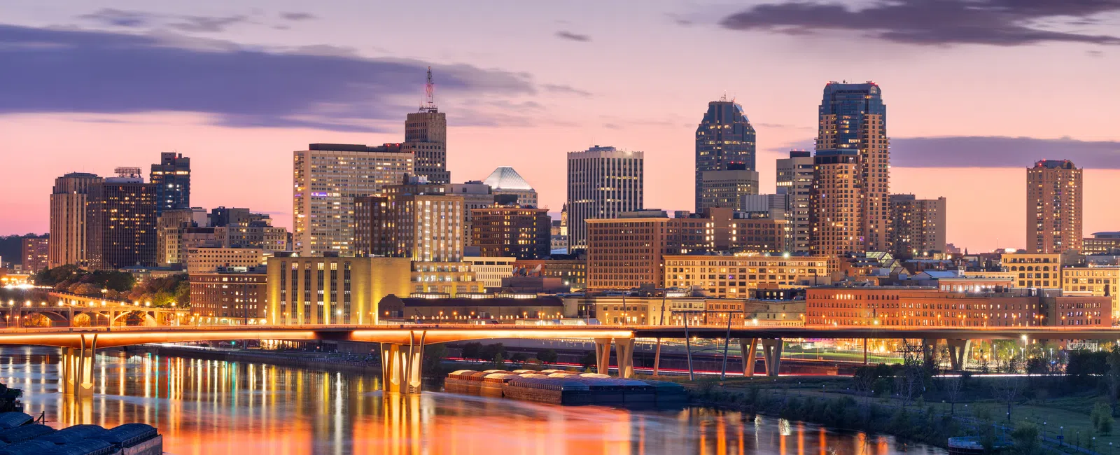 Twilight city skyline with illuminated buildings and bridge reflecting on calm river waters