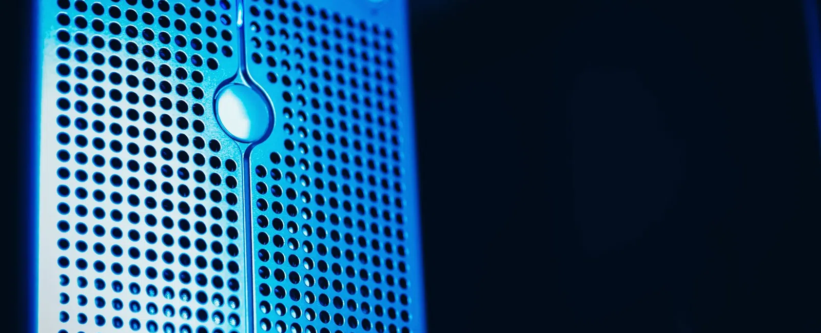 Close-up of a blue-lit computer server tower with perforated metal front panel and control buttons.