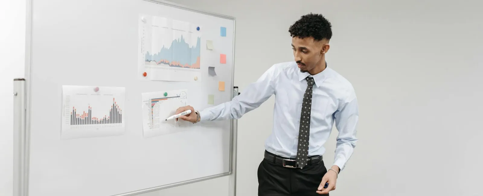 Man in formal attire presenting graphs and charts on a whiteboard during a business meeting.