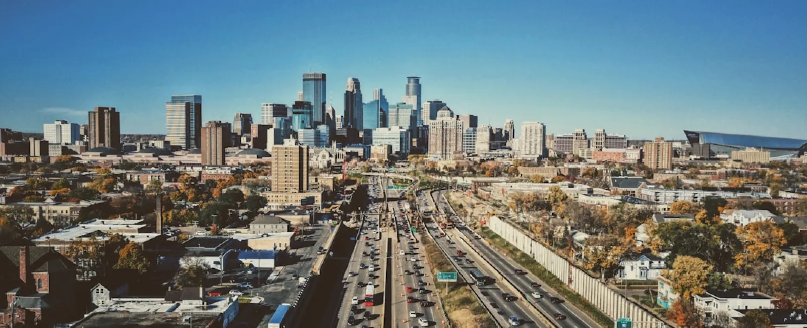 Aerial view of a busy highway leading into a city with skyscrapers under a clear blue sky.