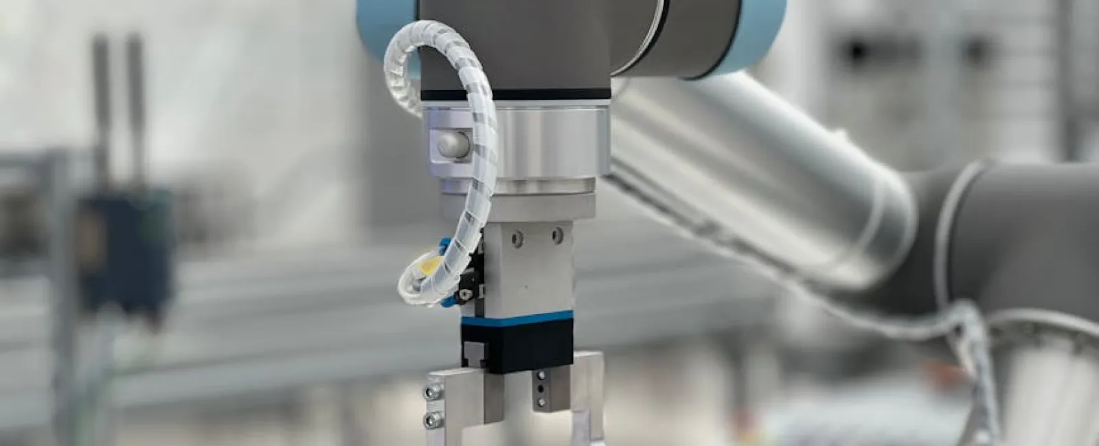 Close-up of a robotic arm with a metal gripper and blue protective covers in a manufacturing setting.