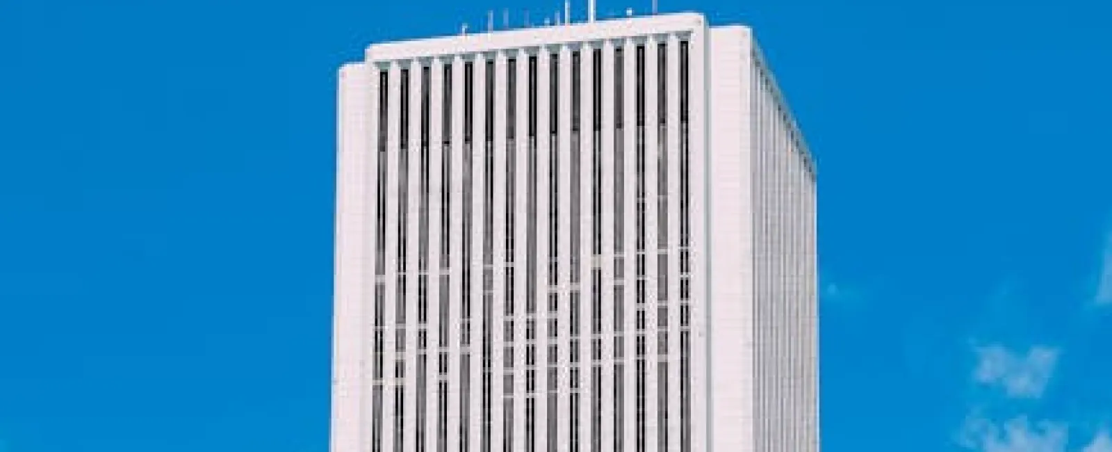 Tall white modern skyscraper with vertical window lines against a bright blue sky with a few clouds.