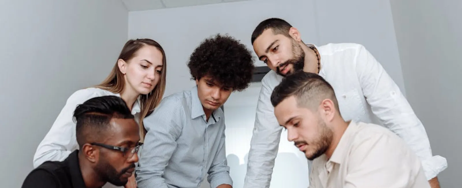 Diverse team of five young professionals gathered around a red notebook collaborating in a modern office.