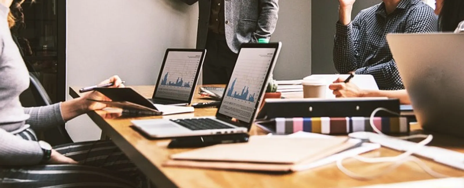Team meeting in modern office with laptops displaying charts and documents on wooden table during collaboration