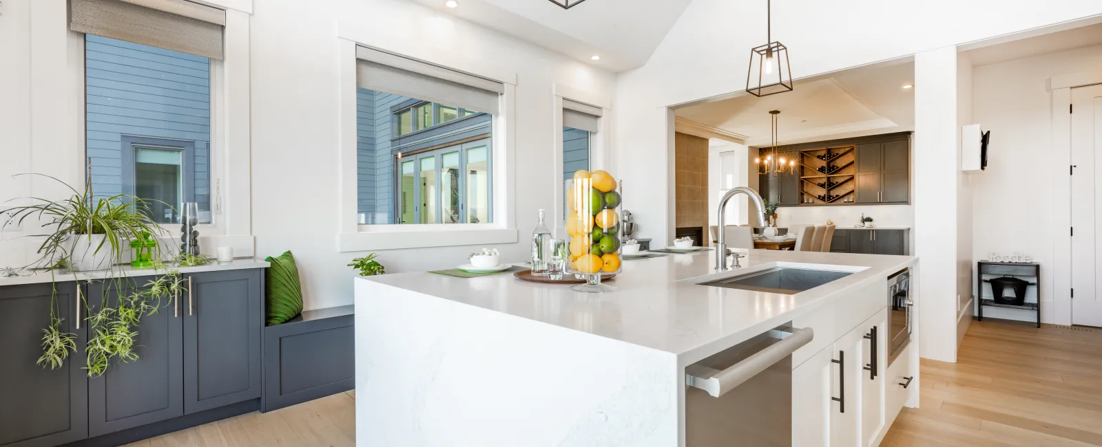 Bright modern kitchen with white marble island, dark cabinets, large windows, and hardwood floors.