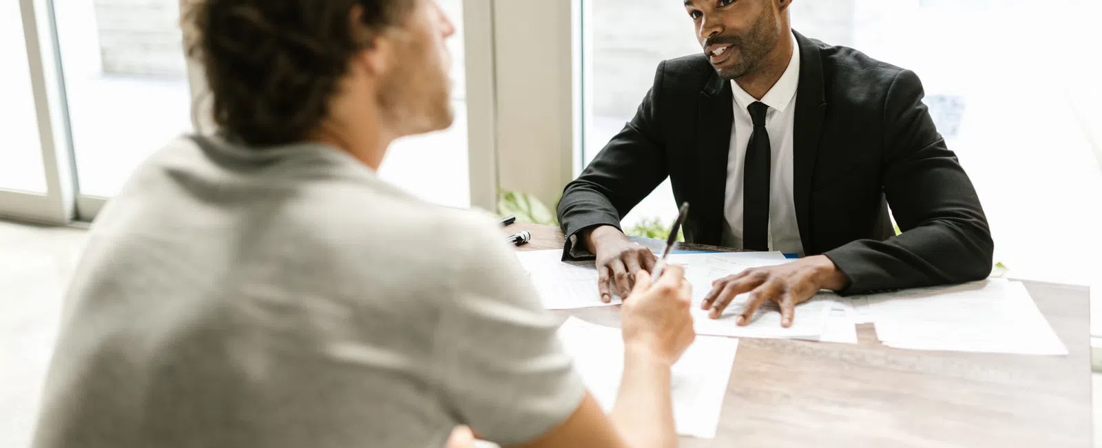 Businessman in suit consulting casually dressed man during a meeting with documents on the table