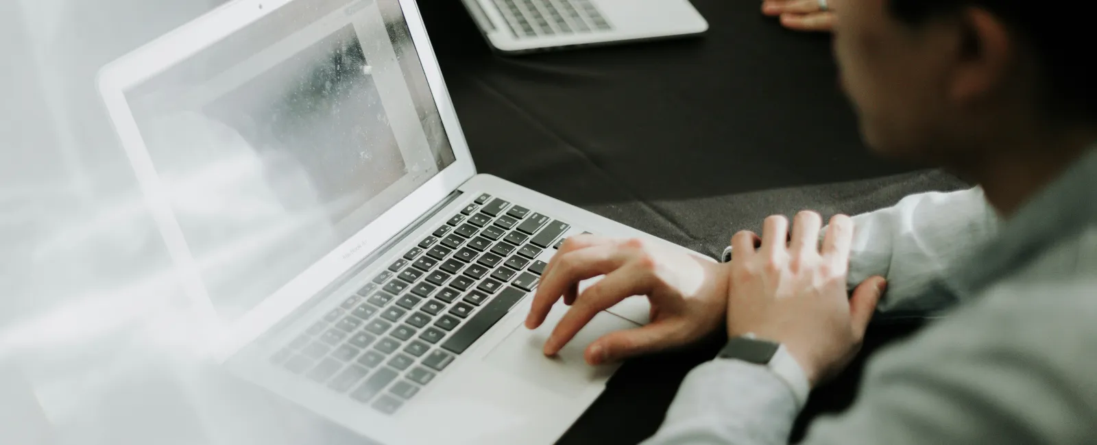 Person using a laptop with another laptop in the background on a black table in a collaborative work setting