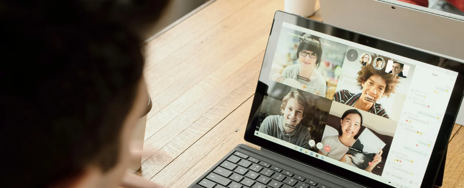 Person using laptop for video conference call with four diverse participants on screen at wooden table