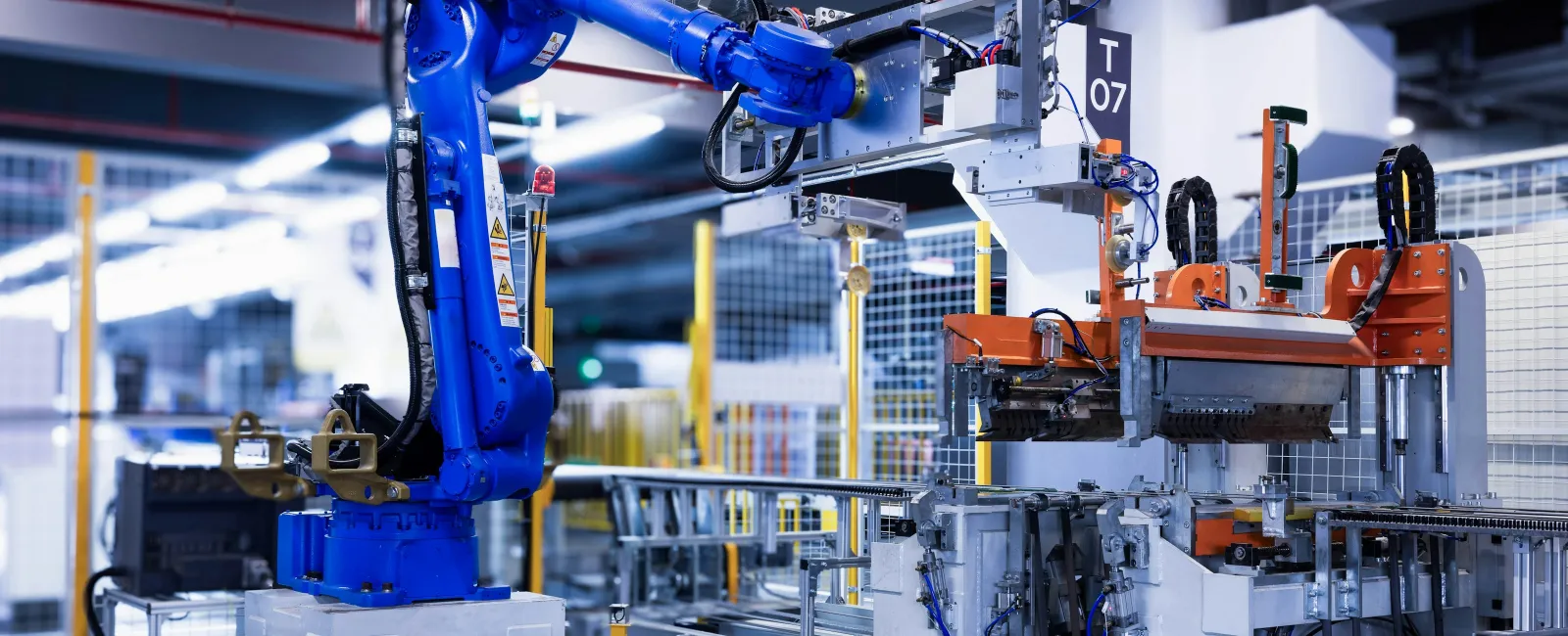 Blue industrial robot arm operating automated machinery in a modern factory with metal components and safety fencing