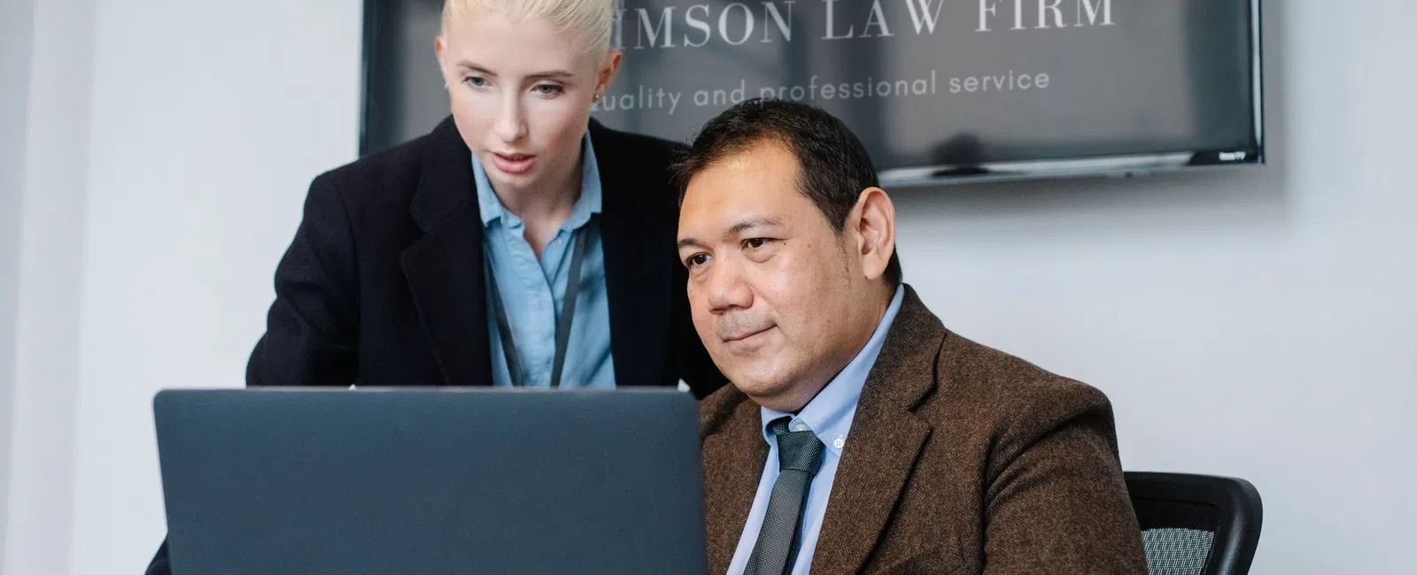 Two lawyers collaborating in an office with a laptop, legal documents, and a judge's gavel on the desk.