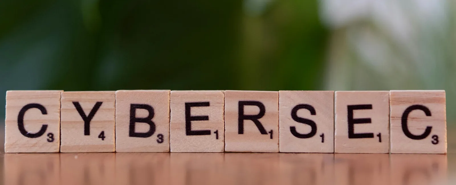 Wooden Scrabble tiles spell out the word CYBERSEC on a wooden surface with a blurred green background