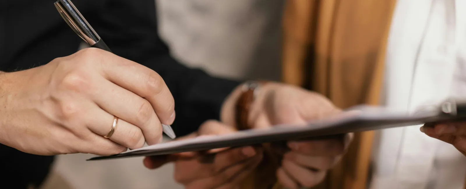 Two professionals in business attire reviewing and signing documents on a clipboard indoors.