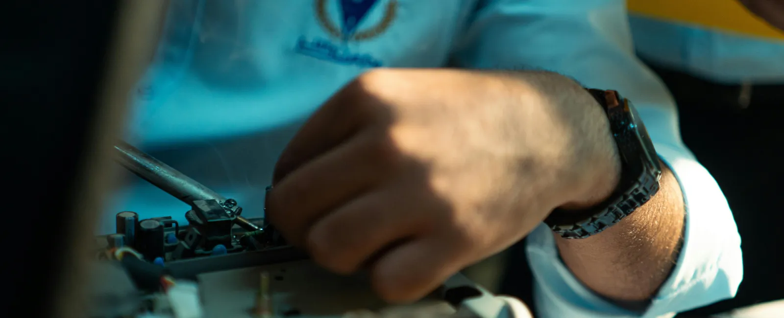 Close-up of a technician's hand repairing electronic equipment, wearing a blue uniform and black watch.